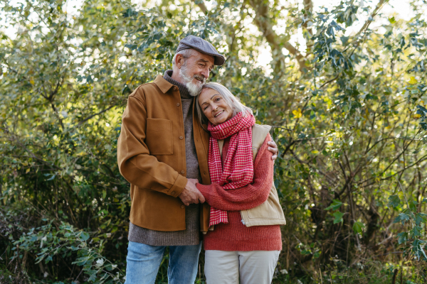 Portrait of beautiful senior couple outdoors in autumn garden. Elderly husband and wife are embracing each other.