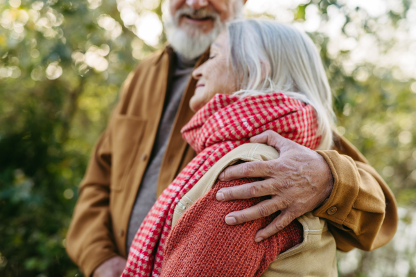 Close up of beautiful senior couple outdoors in autumn garden. Elderly husband and wife are embracing each other.