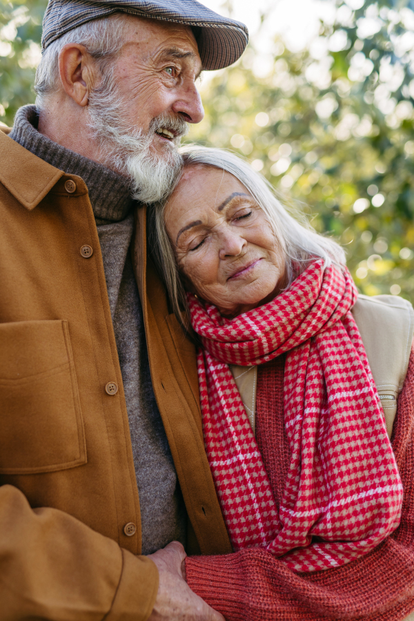 Portrait of beautiful senior couple outdoors in autumn garden. Elderly husband and wife are embracing each other.