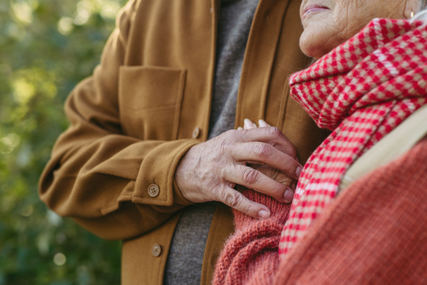 Close up of beautiful senior couple outdoors in autumn garden. Elderly husband and wife are embracing each other.