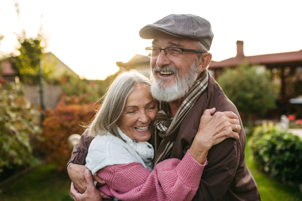 Portrait of beautiful senior couple outdoors in autumn garden. Elderly husband and wife are embracing each other.