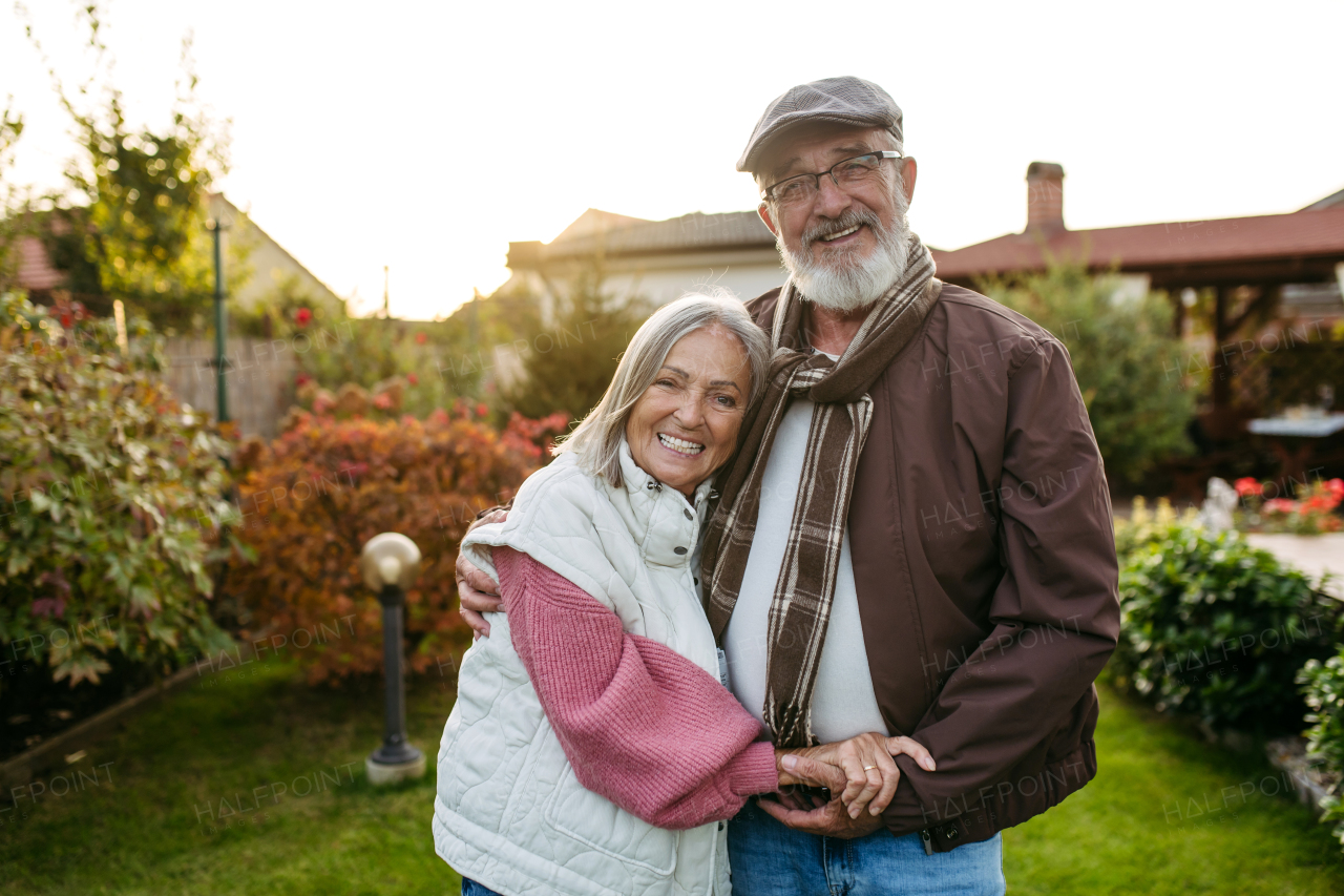 Portrait of beautiful senior couple outdoors in autumn garden. Elderly husband and wife are embracing each other.