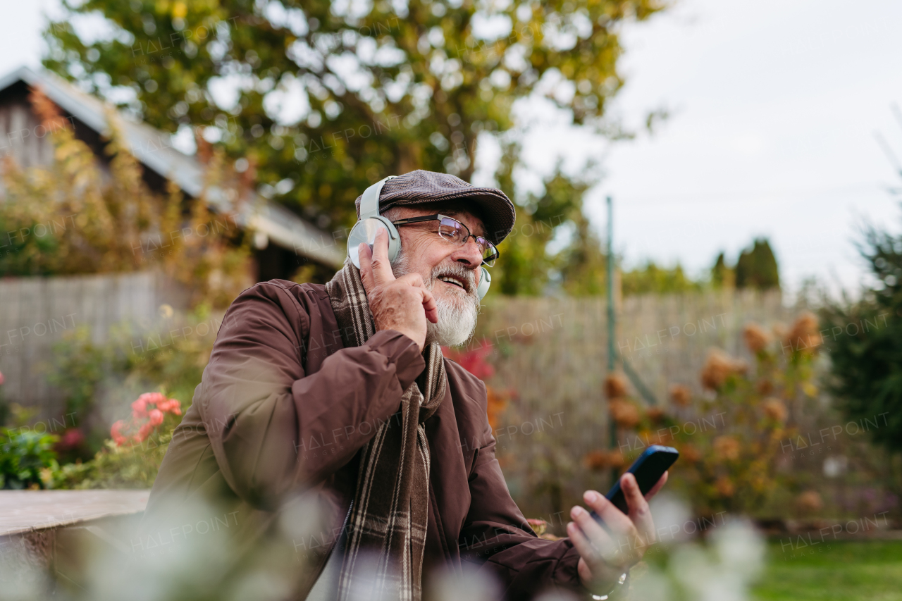 Older man with a gray beard having moment for himself, listening music. Senior wearing headphones and playing music from smartphone