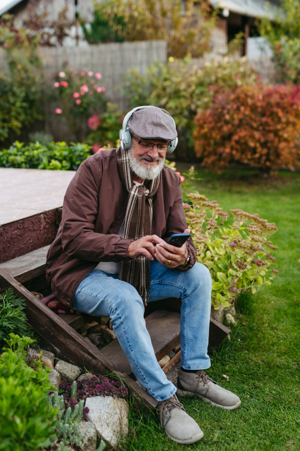 Older man with a gray beard having moment for himself, listening music. Senior wearing headphones and playing music from smartphone