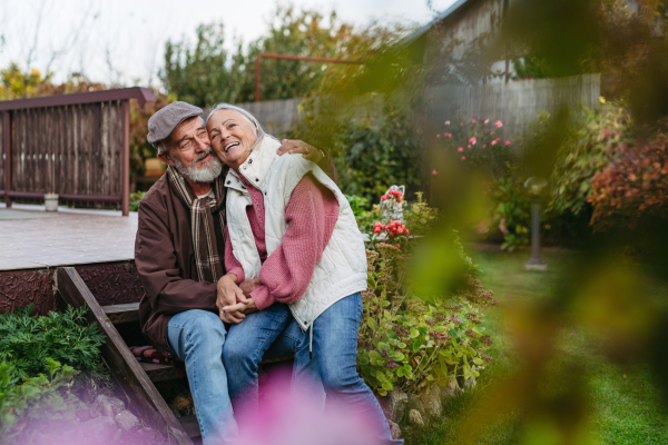 Portrait of beautiful senior couple outdoors in autumn garden. Elderly husband and wife are embracing each other.