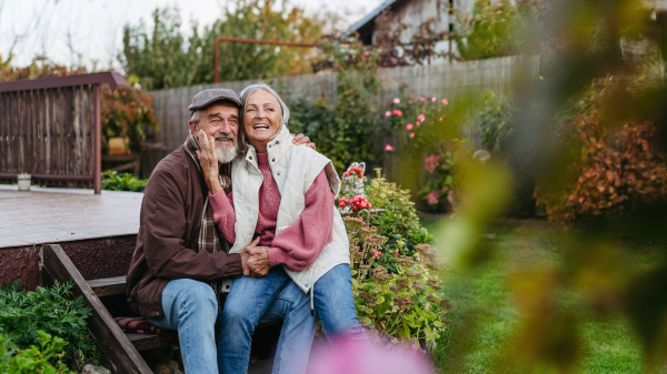 Portrait of beautiful senior couple outdoors in autumn garden. Elderly husband and wife are embracing each other.