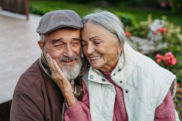 Portrait of beautiful senior couple outdoors in autumn garden. Elderly husband and wife are embracing each other.