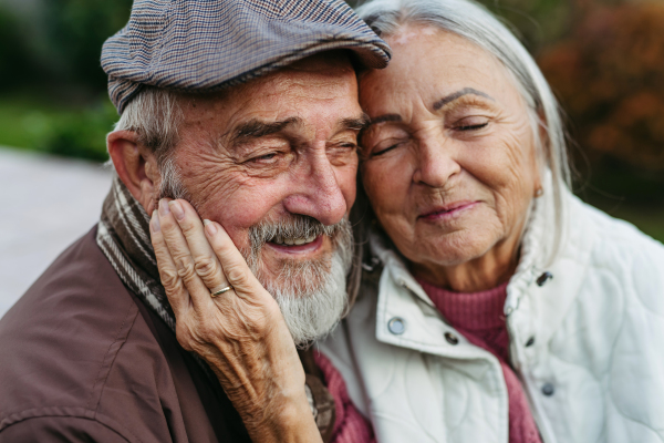 Portrait of beautiful senior couple outdoors in autumn garden. Elderly husband and wife are embracing each other.