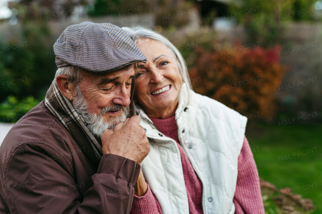 Portrait of beautiful senior couple outdoors in autumn garden. Elderly husband and wife are embracing each other.