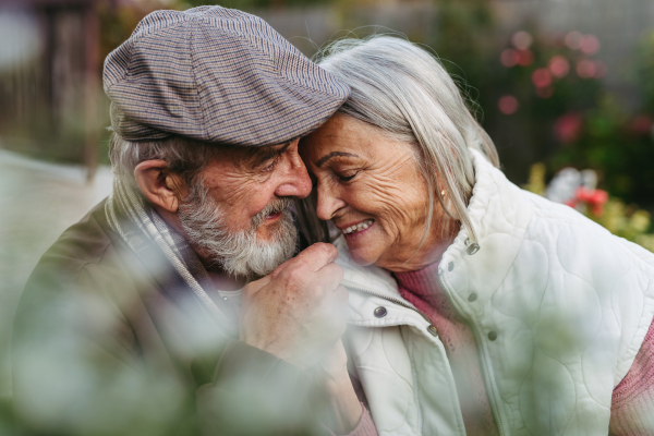 Portrait of beautiful senior couple outdoors in autumn garden. Elderly husband and wife are embracing each other.