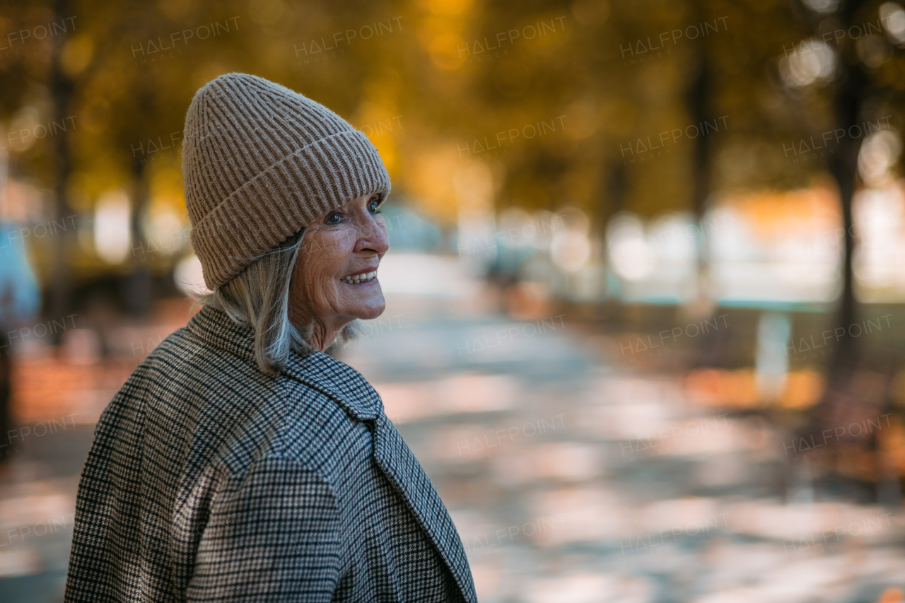 Portrait of a beautiful senior woman standing outdoors, autumn park behind her