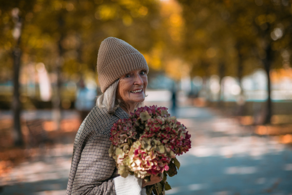 Portrait of a beautiful senior woman standing outdoors with bouquet of dried flowers. Autumn park behind her