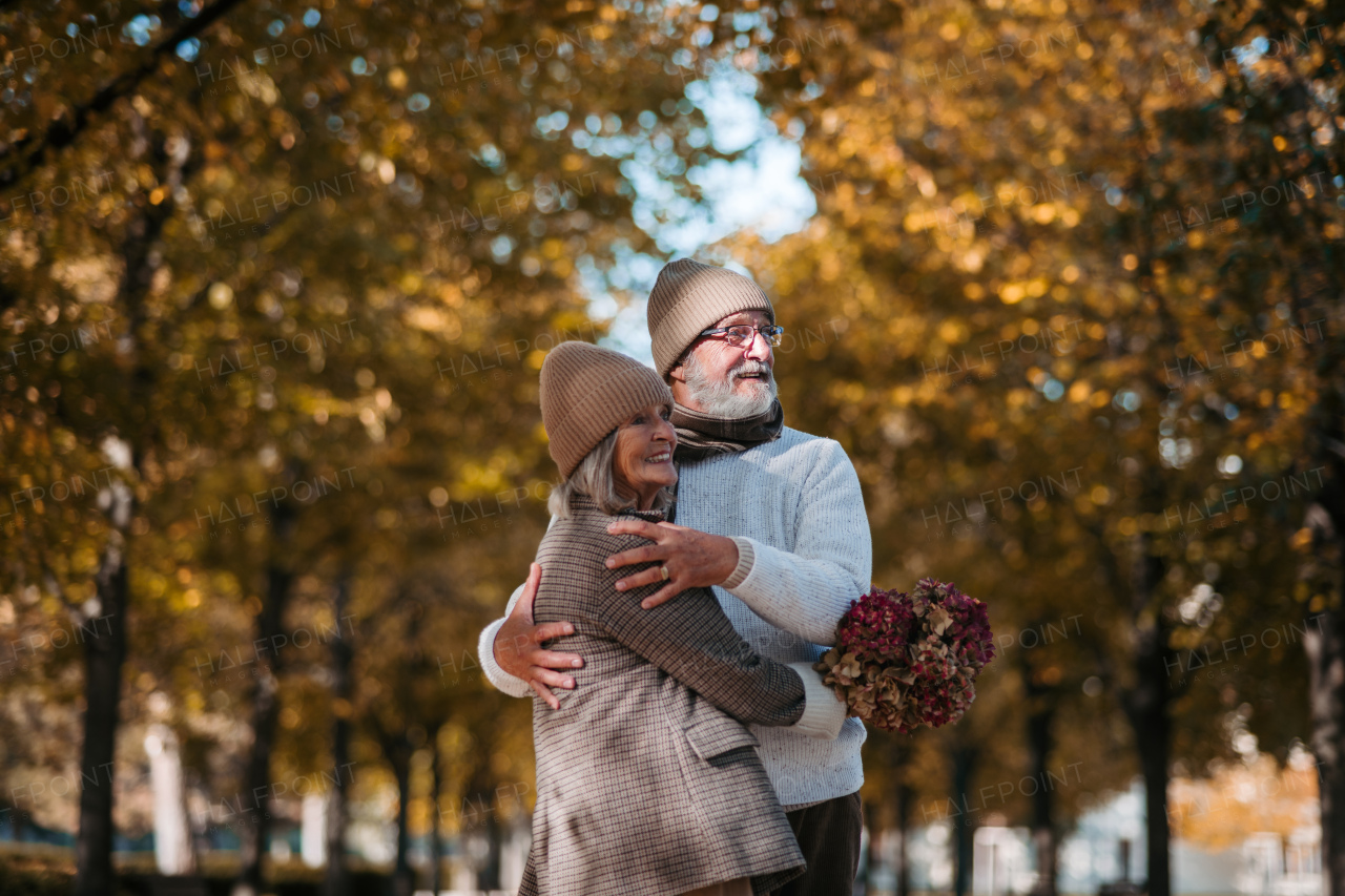 Beautiful senior couple during walk in autumn park. Elderly husband and wife are embracing each other.