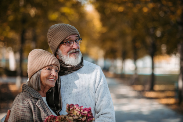 Beautiful senior couple during walk in autumn park. Elderly husband and wife are embracing each other.