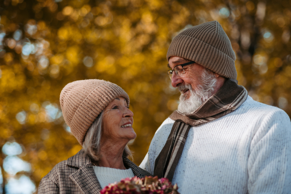 Portrait of beautiful senior couple during walk in autumn park. Elderly husband and wife are looking at each other lovingly