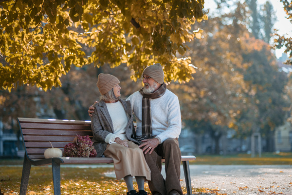 Beautiful senior couple sitting on bench in autumn park. Elderly husband and wife looking at each other lovingly.