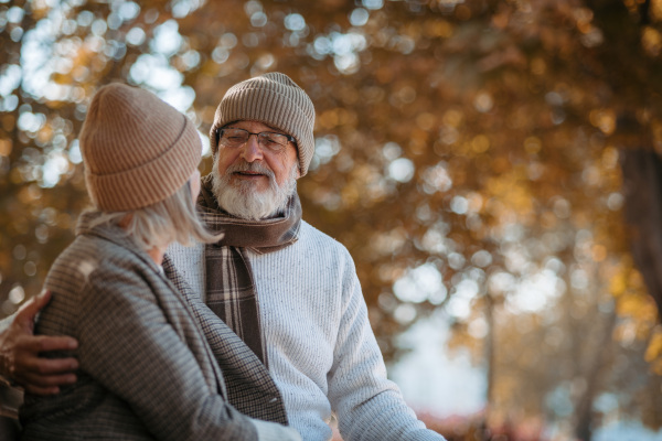 Beautiful senior couple sitting on bench in autumn park. Elderly husband and wife looking at each other lovingly.