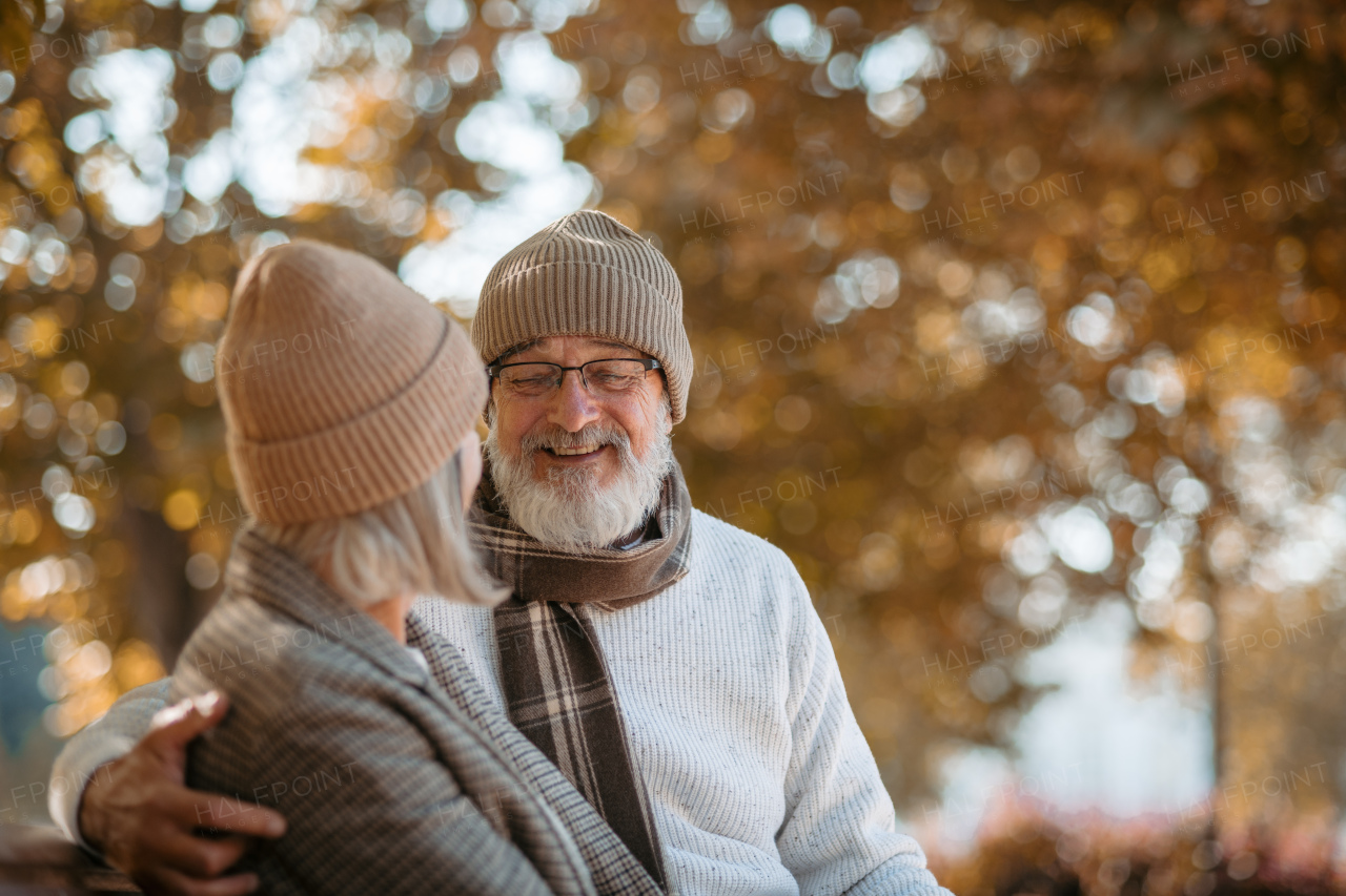 Beautiful senior couple sitting on bench in autumn park. Elderly husband and wife looking at each other lovingly.