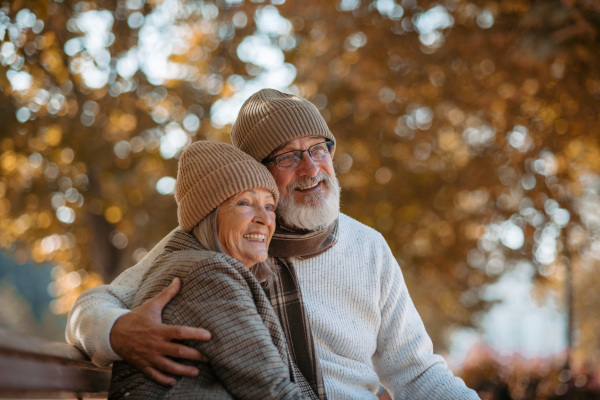 Beautiful senior couple during walk in autumn park. Elderly husband and wife are embracing each other.