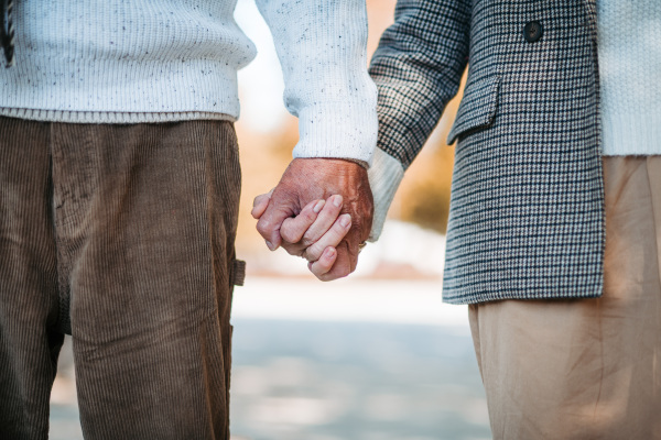 Close up of holding hands of senior couple during walk in autumn park