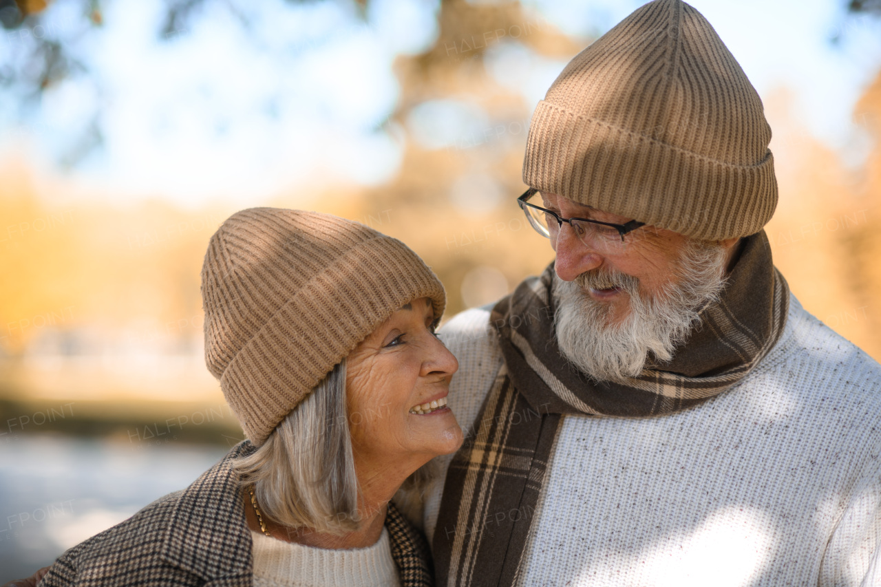 Beautiful senior couple during walk in autumn park. Elderly husband and wife are embracing each other.