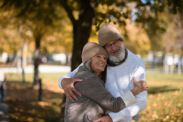 Beautiful senior couple during walk in autumn park. Elderly husband and wife are embracing each other.