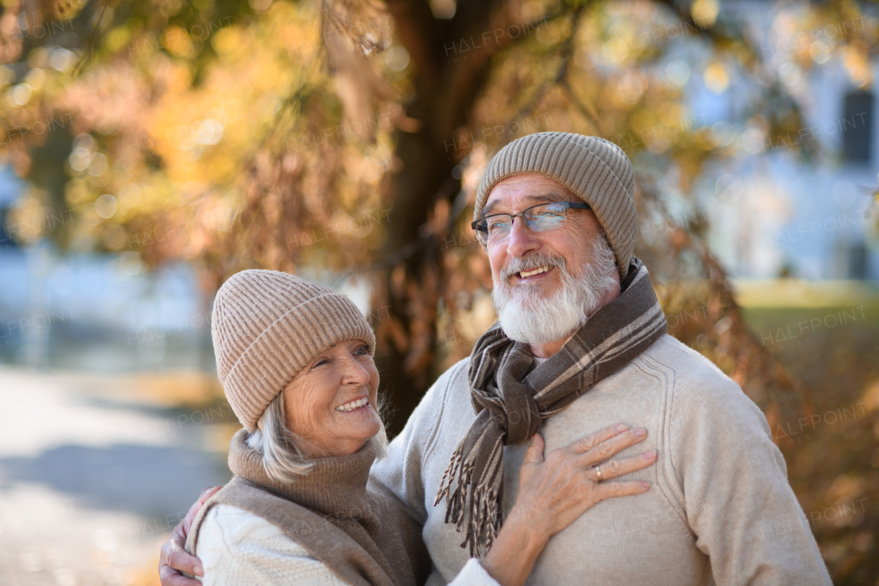 Beautiful senior couple during walk in autumn park. Elderly husband and wife are embracing each other.