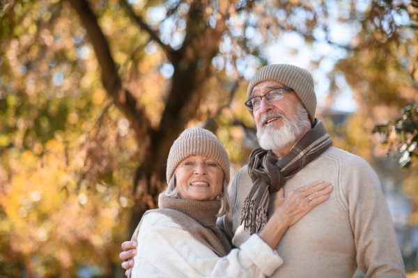 Beautiful senior couple during walk in autumn park. Elderly husband and wife are embracing each other.