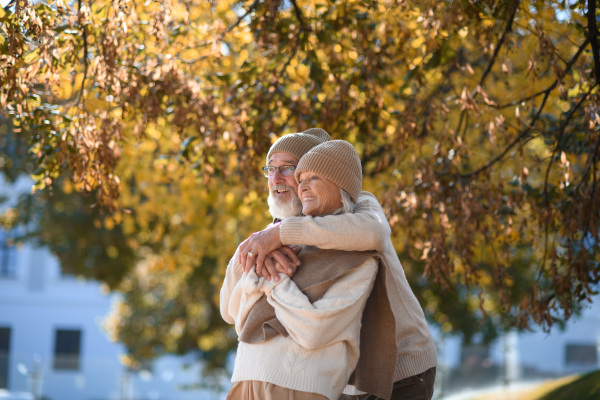 Beautiful senior couple during walk in autumn park. Elderly husband and wife are embracing each other.