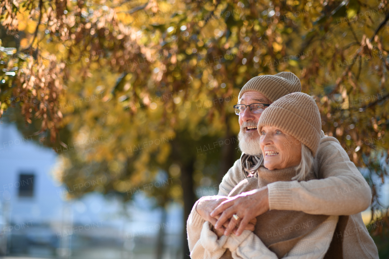 Beautiful senior couple during walk in autumn park. Elderly husband and wife are embracing each other.