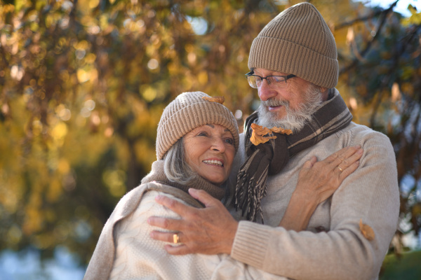 Beautiful senior couple during walk in autumn park. Elderly husband and wife are embracing each other.