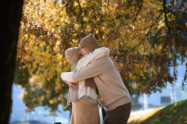 Beautiful senior couple during walk in autumn park. Elderly husband and wife are embracing each other.