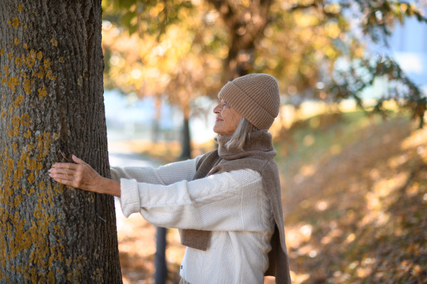 Portrait of a beautiful senior woman with headphones in autumn park, listening music with closed eyes.