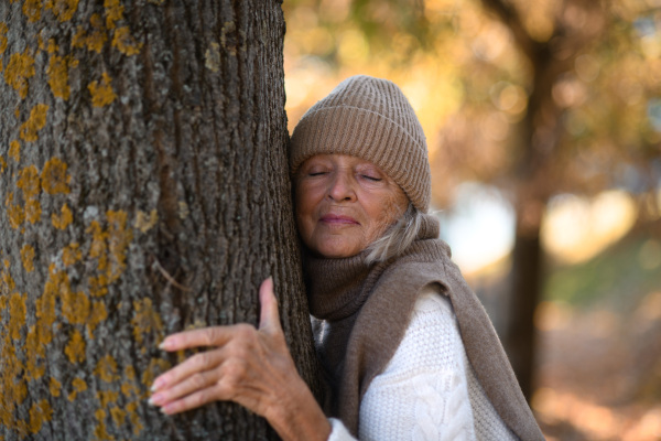 Portrait of a beautiful senior woman with headphones in autumn park, listening music with closed eyes.