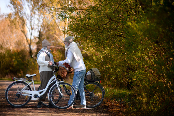 Elderly couple on walk in park, pushing their bikes side by side. Seniors in love on stroll through autumn city, enjoying a peaceful moment.