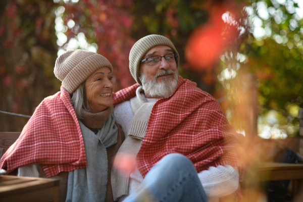 Elderly married couple sitting on a coffee shop terrace on beautiful autumn day, enjoying cup of coffee in autumn atmosphere.