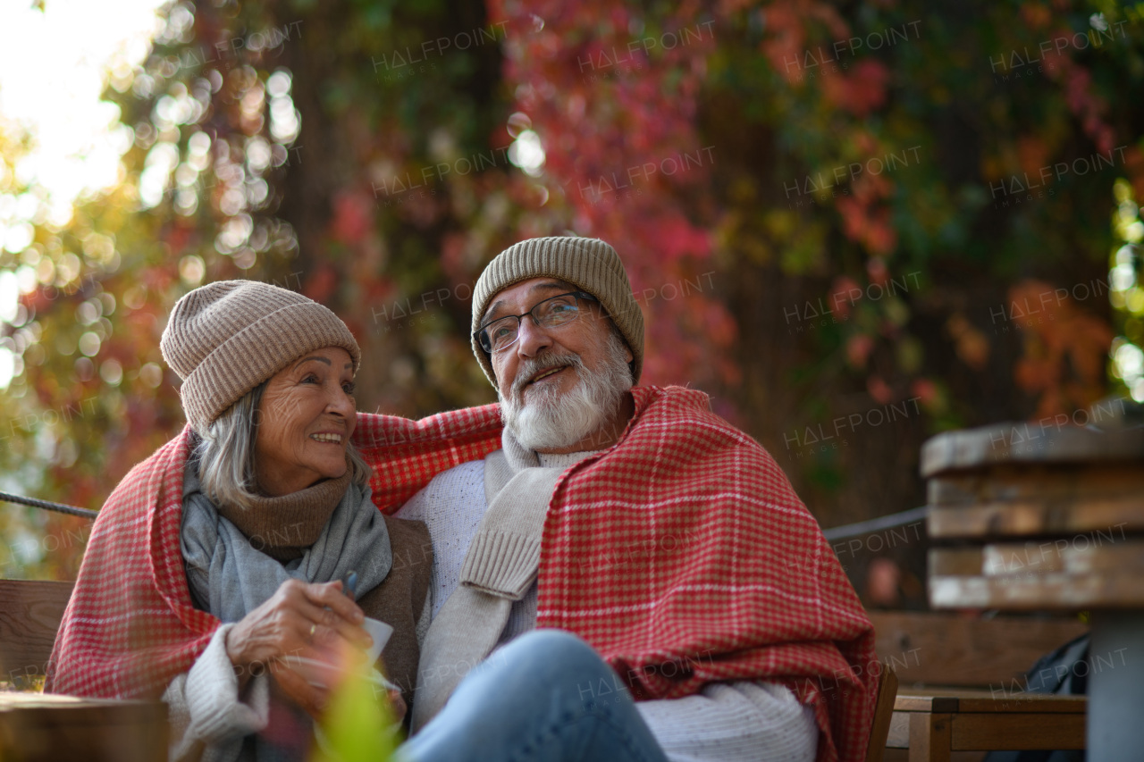 Elderly married couple sitting on a coffee shop terrace on beautiful autumn day, enjoying cup of coffee in autumn atmosphere.