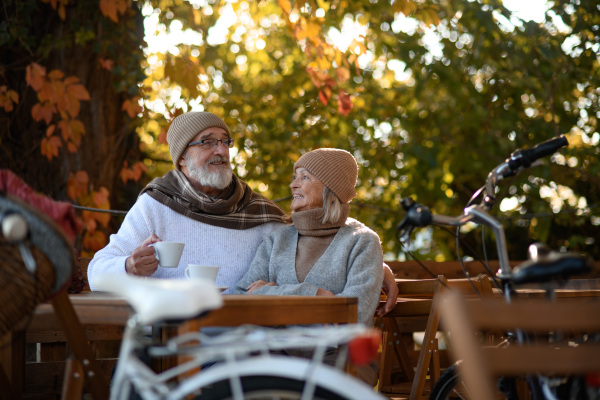 Elderly married couple sitting on a coffee shop terrace on beautiful autumn day, enjoying cup of coffee in autumn atmosphere.