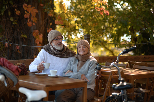 Elderly married couple sitting on a coffee shop terrace on beautiful autumn day, enjoying cup of coffee in autumn atmosphere.