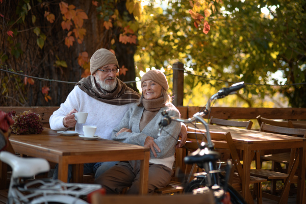 Elderly married couple sitting on a coffee shop terrace on beautiful autumn day, enjoying cup of coffee in autumn atmosphere.