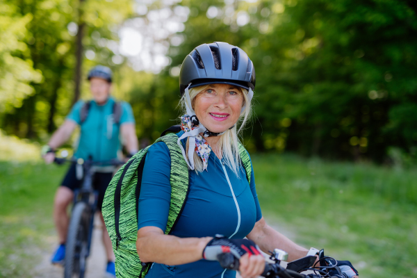 Portrait of an active senior couple riding bicycles at summer park, woman is looking at camera, healthy lifestyle concept.