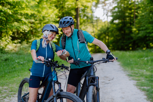 A portrait of active senior couple riding bicycles at summer park, looking at sports smartwatch, checking their performance.