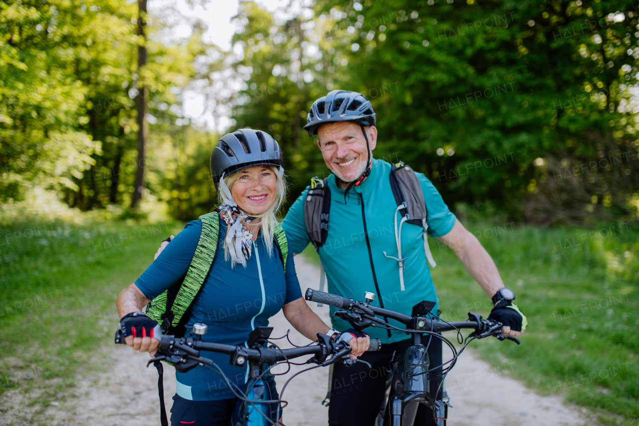 A portrait of active senior couple riding bicycles at summer park, standing on path and looking at camera