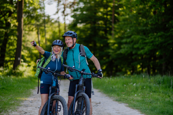 A portrait of active senior couple riding bicycles at summer park, standing on path and looking at camera