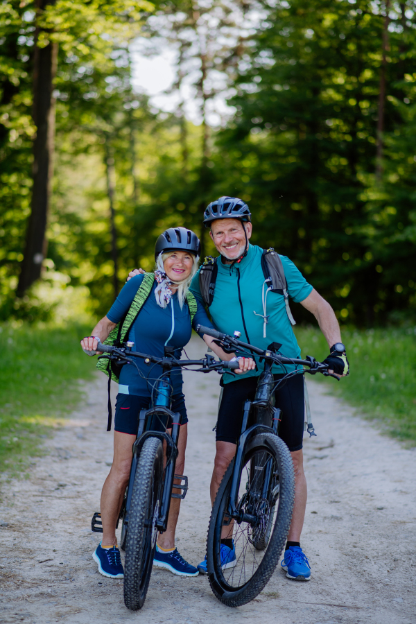 A portrait of active senior couple riding bicycles at summer park, standing on path and looking at camera