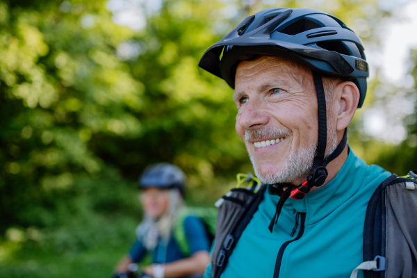 aN Active senior couple riding bicycles at summer park, man with bicycle helmet, healthy lifestyle concept.