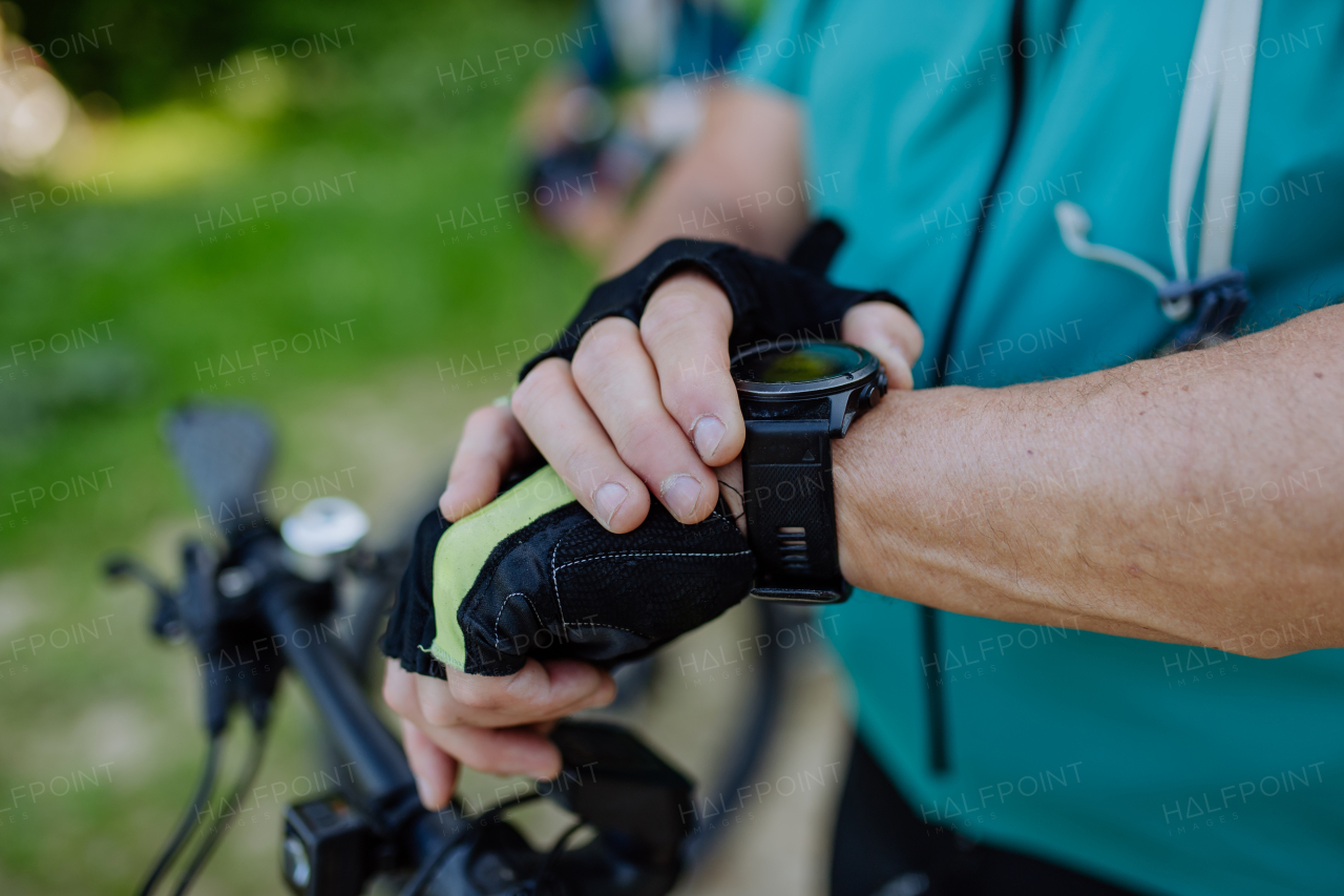 A close-up of senior man biker setting and looking at sports smartwatch, checking his performance.