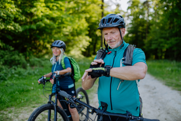 A portrait of active senior couple riding bicycles at summer park, looking at sports smartwatch, checking their performance.