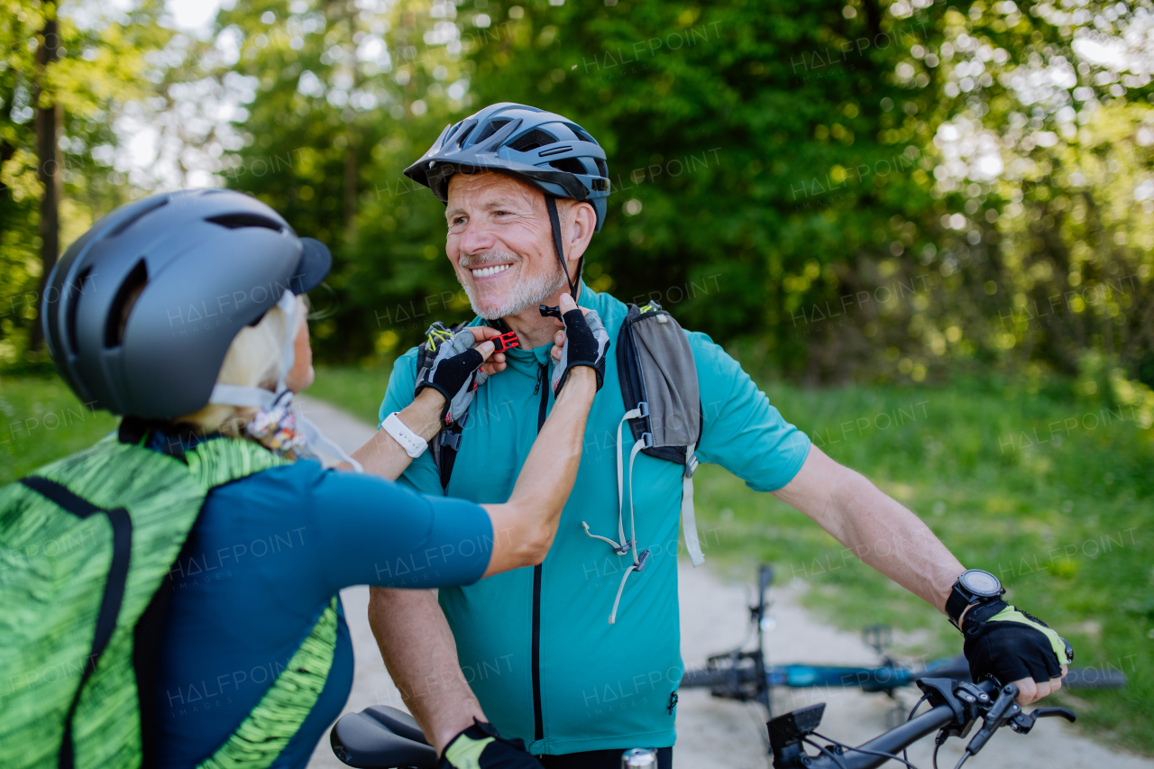 AAn ative senior couple riding bicycles at summer park, putting on helmet, healthy lifestyle concept.