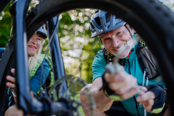 An active senior couple repairing bicycle, pumping up tire in nature in summer.